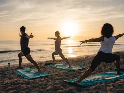 Tres personas practican yoga en la playa al amanecer.
