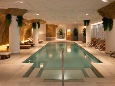 Piscina interna con lettini e pareti in stile pietra in un'area benessere.