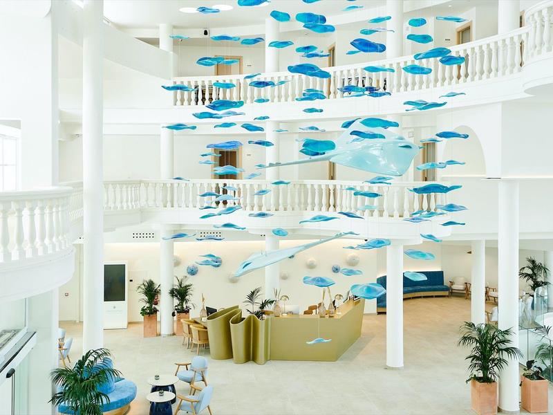 Area lounge luminosa in hotel con installazione moderna di pesci blu al soffitto.