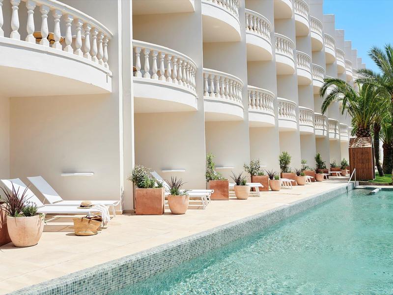 Piscina moderna in hotel con lettini e palme in un ambiente soleggiato e rilassante.