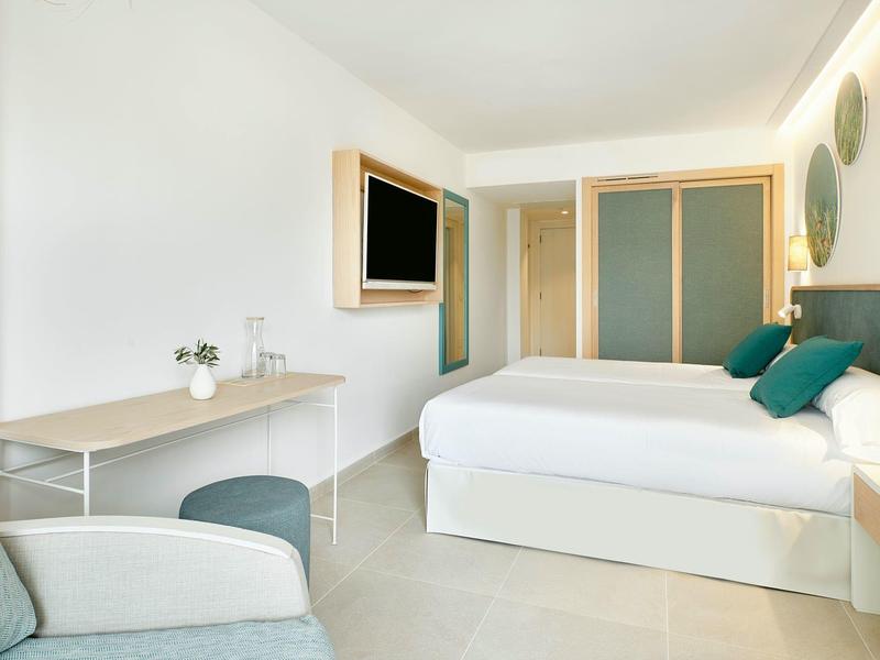 Camera d'hotel luminosa con letto matrimoniale, scrivania, sedia e TV a parete.