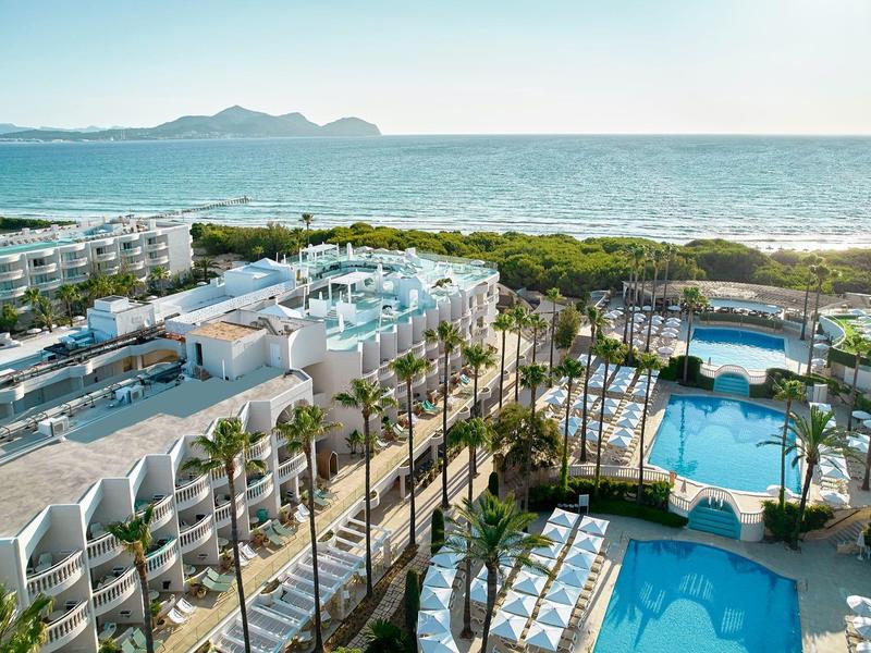 Complesso alberghiero con piscine, palme e vista sul mare sotto un cielo limpido.