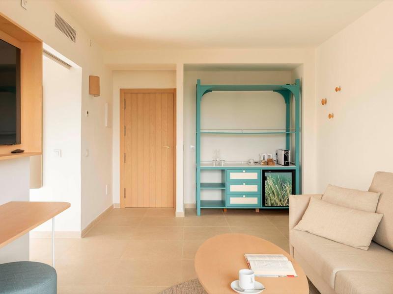 Zona luminosa e minimalista della camera d'hotel con divano, tavolo e armadio aperto.