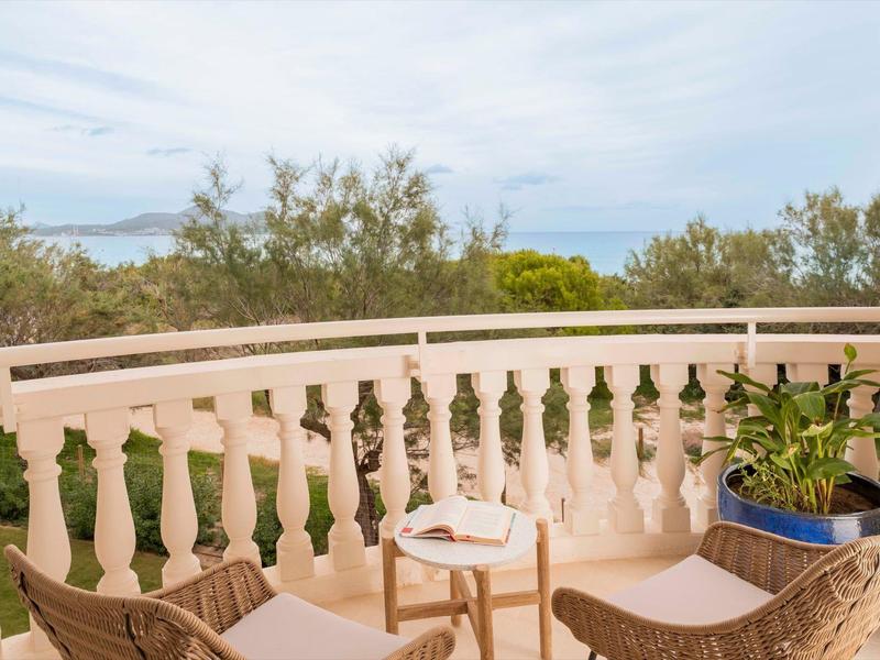 Balcone con sedie, tavolo e piante con vista sul mare e sugli alberi.