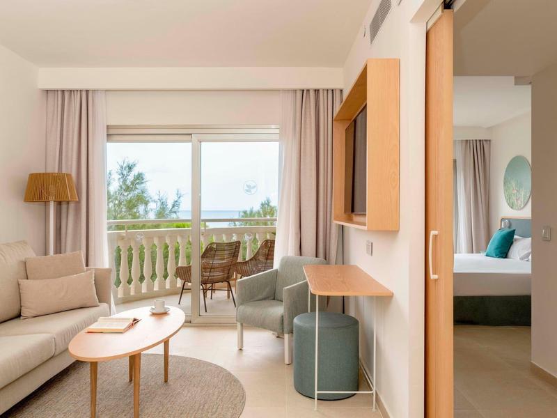 Soggiorno luminoso con divano, tavolini e balcone con vista sul verde.