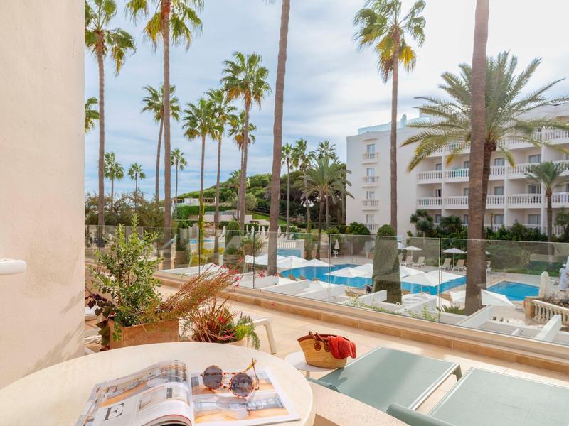 Vista sulla piscina dell'hotel con palme e sdraio in una giornata di sole.