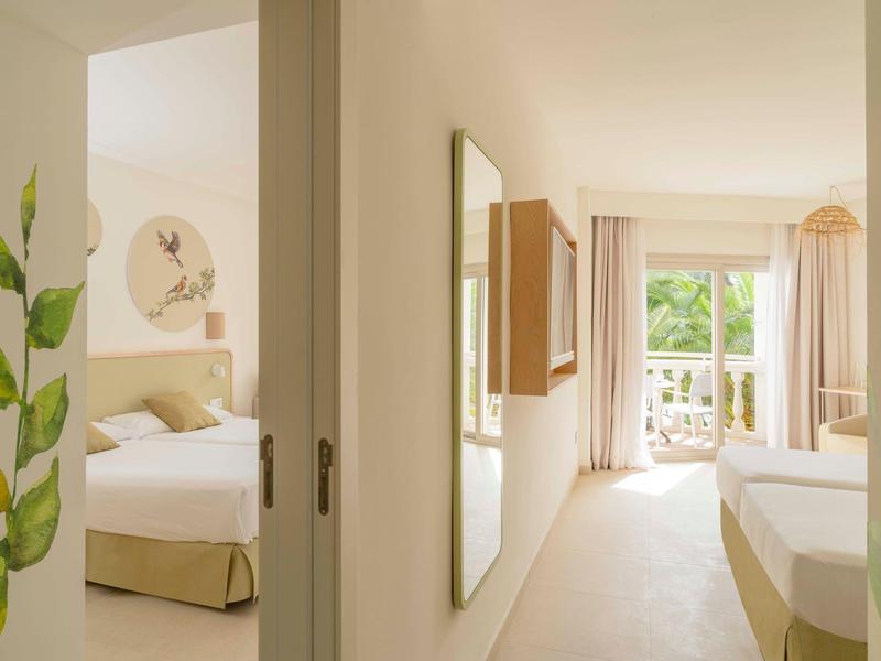 Camera d'hotel luminosa con due letti, balcone e stanza adiacente con letto singolo.