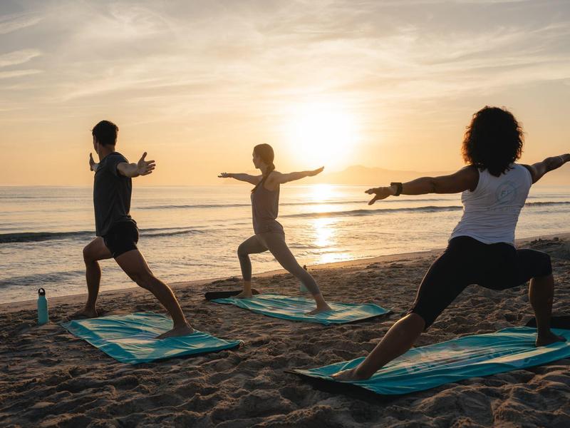 Tre persone praticano yoga sulla spiaggia all'alba.