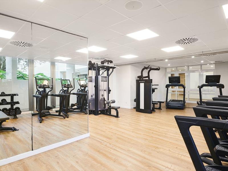 Palestra luminosa con pavimento in legno, parete a specchio e vari attrezzi da allenamento.