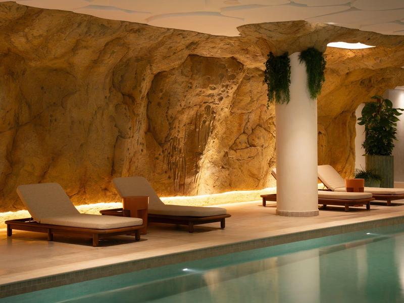 Piscina interna con lettini davanti a una parete rocciosa e piante.