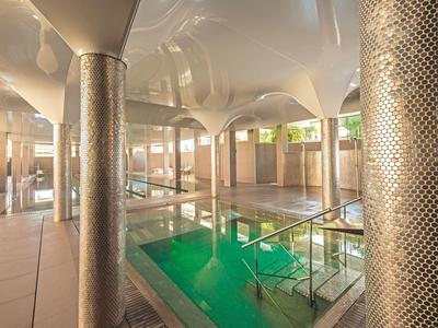 Innenbereich eines Pools mit großen Säulen, glatten Böden und grünlichem Wasser.
