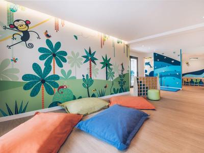 Kinderspielbereich mit bunten Kissen, Wandmalerei mit Blumen und Affe, hell und freundlich gestaltet.