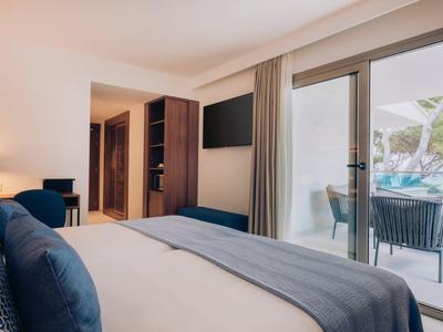Modernes Hotelzimmer mit Doppelbett, Fernseher, Sitzbereich und Balkon mit Blick auf Pool.