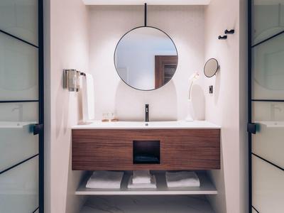 Modernes Badezimmer mit rundem Spiegel, Waschbecken, Holzunterschrank und weißen Handtüchern.