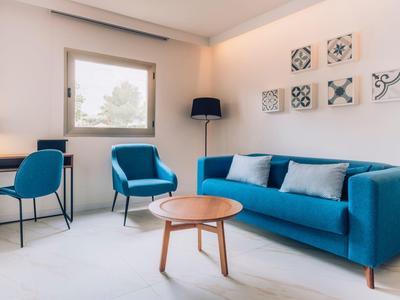 Helles Wohnzimmer mit blauem Sofa, Sesseln, Holztisch und Wanddeko über dem Sofa.