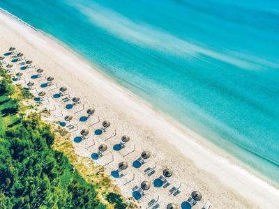 Luftaufnahme eines Strandes mit Reihen von Sonnenschirmen und Liegestühlen neben türkisfarbenem Meer.