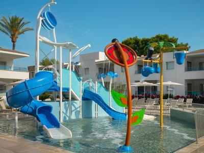 Kinderspielplatz mit bunten Wasserrutschen und Wasserspielen vor weißem Ferienhaus bei Sonnenschein.