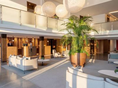 Moderna hall di un hotel con poltrone bianche eleganti e grandi piante in uno spazio luminoso.