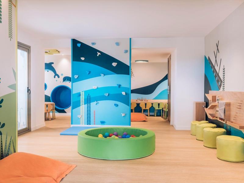 Sala de juegos infantil colorida con área de asientos suaves y murales en el hotel.