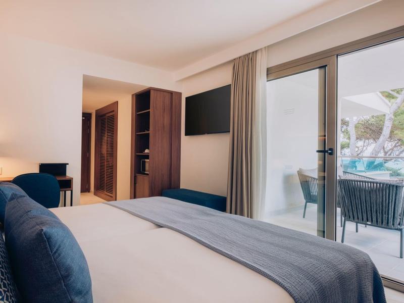 Habitación de hotel moderna con cama grande, TV y balcón con vista a muebles de terraza y jardín.