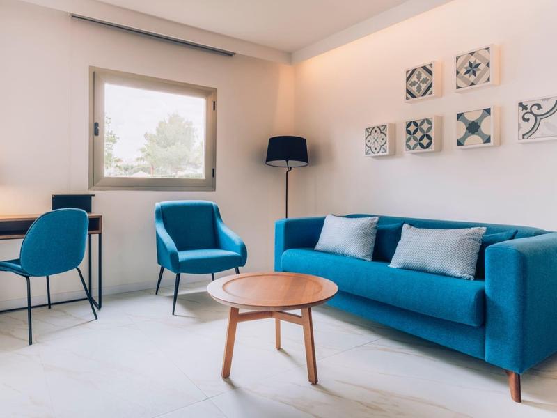 Sala moderna con sofá azul, sillones, mesa redonda de madera y pared blanca con decoración.