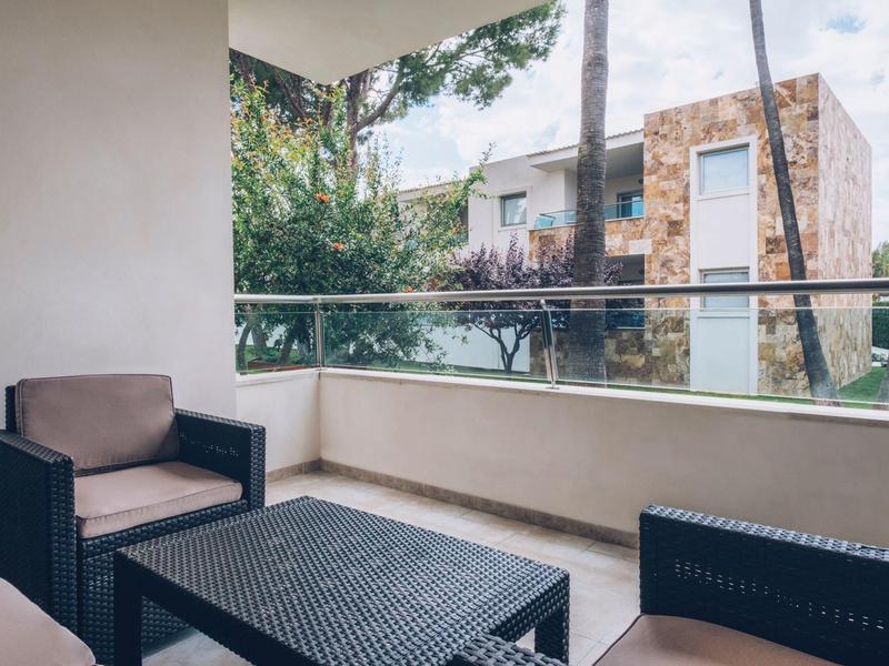 Balcón con muebles negros y vista a árboles y una pared de piedra al fondo.