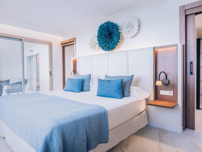 Habitación de hotel luminosa con cama grande, cojines azules y decoración mural azul.