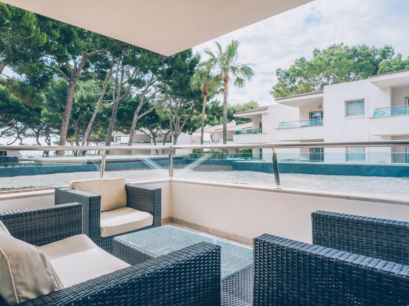 Terraza con muebles de ratán y vista a la piscina y árboles en un complejo hotelero.