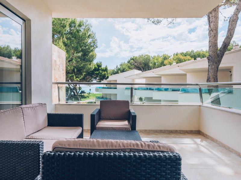 Balcón con muebles modernos de rattán y barandilla de vidrio con vista a un área arbolada.