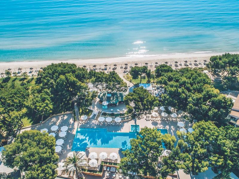 Vista aérea de un hotel de playa con piscina, tumbonas y vista al mar azul.