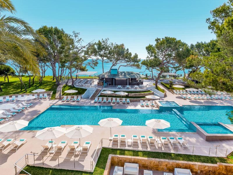 Piscina al aire libre moderna con tumbonas y vista al mar en un complejo hotelero.