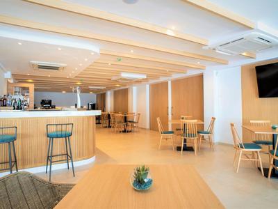 Área de restaurante moderna y luminosa con mesas, sillas y barra en tonos madera clara y blanca.