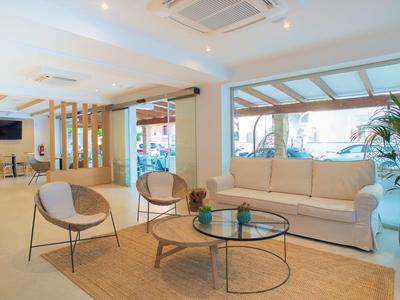 Habitación de hotel luminosa con sofá, sillas, mesa de centro de vidrio y grandes ventanas con vista al exterior.