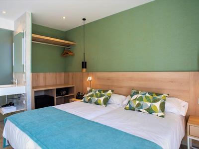 Habitación de hotel moderna con cama doble, pared verde, detalles de madera y colchas azules.