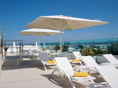 Sillas de descanso modernas con cojines amarillos y sombrillas en una terraza en la azotea con vista al mar.