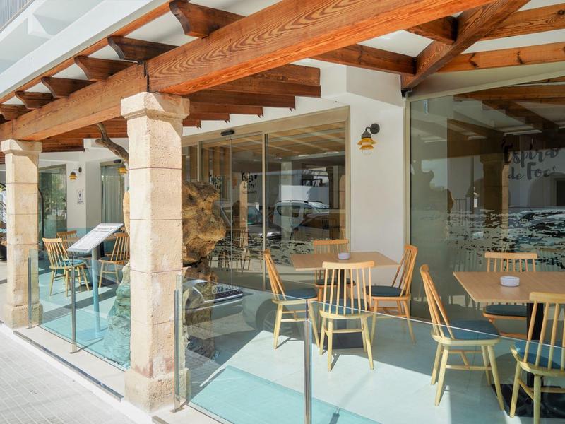 Área exterior moderna de un hotel con barandilla de vidrio y muebles de madera bajo techo de madera.