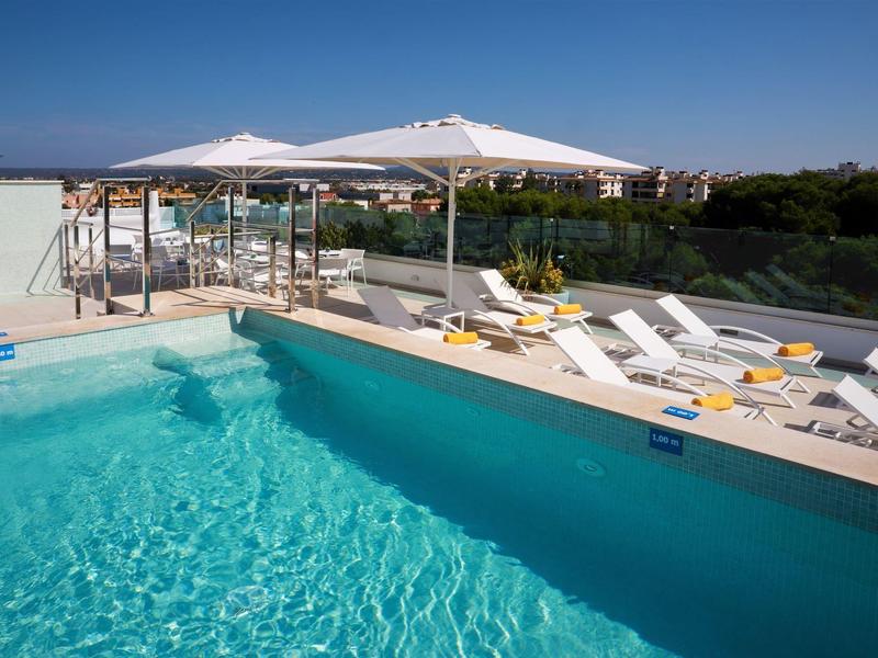 Piscina al aire libre con tumbonas y sombrillas blancas en hotel soleado.