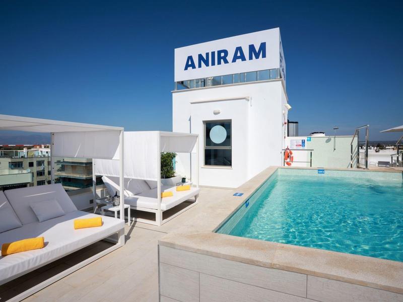Piscina moderna de hotel con camas lounge y agua azul clara bajo cielo despejado.