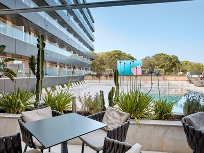 Área exterior moderna de un hotel con asientos, plantas y vista a la zona de la piscina.