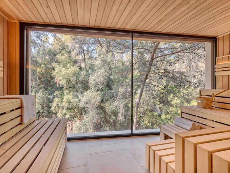 Sauna con revestimiento de madera y gran ventanal con vista a los árboles.