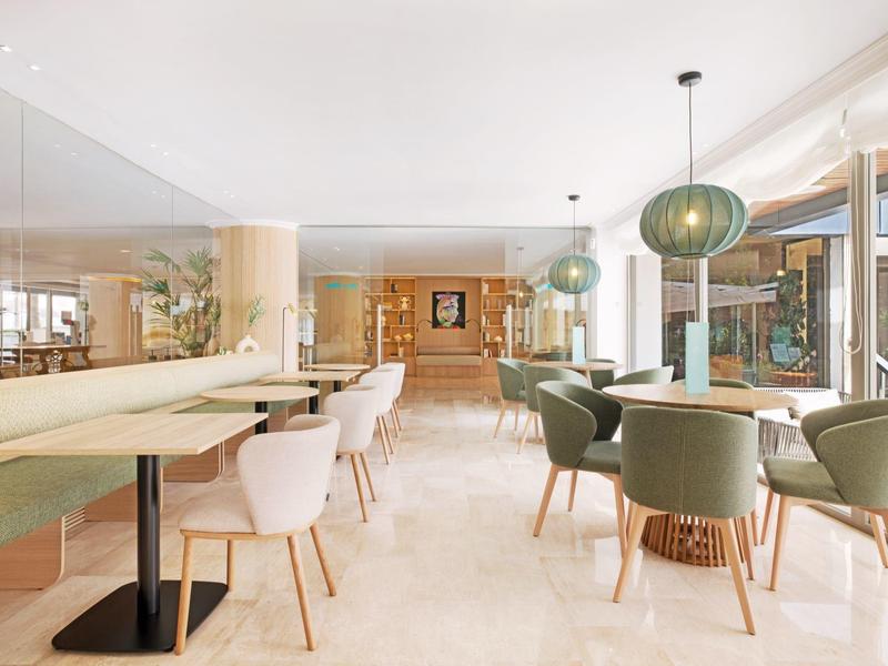 Área de restaurante de hotel con decoración clara, sillas modernas y grandes ventanales.