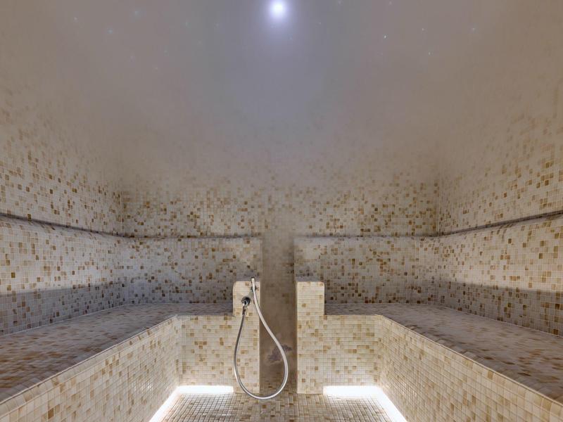 Interior de una sauna mosaico con bancos y una ducha en el centro.