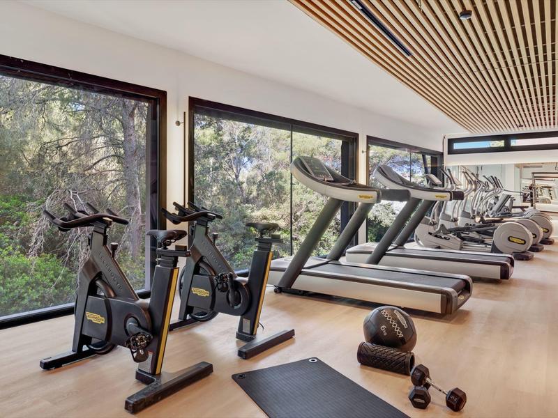 Gimnasio moderno con cintas de correr, bicicletas y grandes ventanas con vista al área verde.