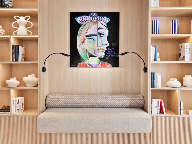 Habitación de hotel moderna con sofá empotrado, estanterías con decoración y colorida obra de arte abstracta en la pared.
