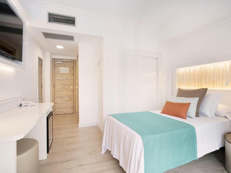 Habitación de hotel luminosa con cama doble, diseño moderno y suelo de madera.