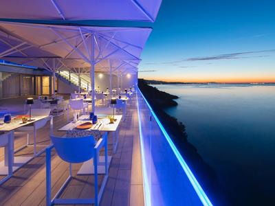 Modern restaurant met blauw verlichte terras en uitzicht op rustige zee bij zonsondergang