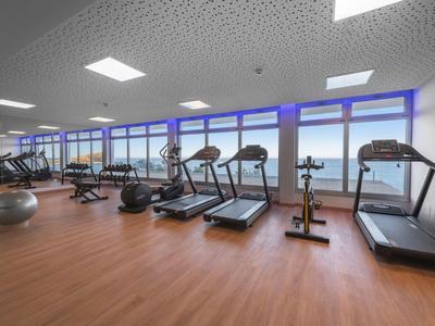 Moderne sportschool met loopbanden en vloerfitnessapparatuur op houten vloer en grote ramen.