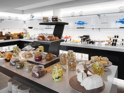 Moderní snídaňový bufet se sýry, chlebem a pomazánkami v světlé místnosti.