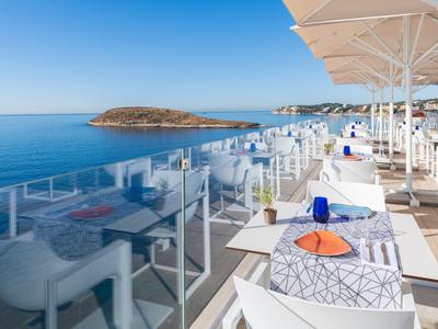 Terasa restaurace u moře s výhledem na malý ostrov pod jasnou oblohou.