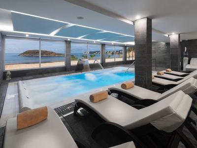 Moderní vnitřní bazén s lehátky a panoramatickými okny s výhledem na moře.